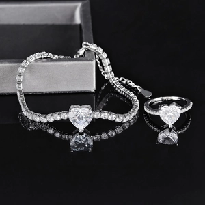 Macro shot of silver heart-shaped zircon ring and tennis bracelet on black reflective base