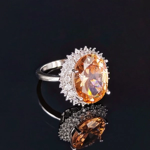 Luxurious oval orange zircon ring in silver finish with sparkling halo on black reflection