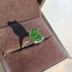 Macro detail of rectangle emerald ring with pavé diamond band in a velvet jewelry box