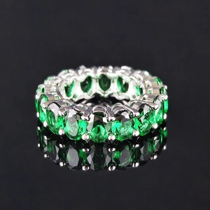 Anillo de plata brillante con circones verdes ovalados sobre un fondo negro reflectante