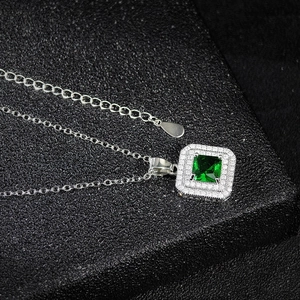 Macro shot of silver necklace featuring square emerald pendant with halo setting and O-chain