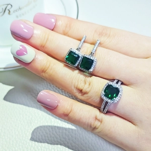 Detailansicht des Sets aus Ring und Ohrringen mit grünem Smaragdschliff an der Hand