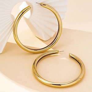 Detailed macro view of high-polished gold bamboo hoop earrings on a textured fan background