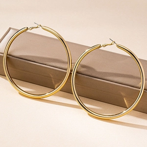 Polished gold bamboo hoop earrings displayed on a brown jewelry box in a studio setting