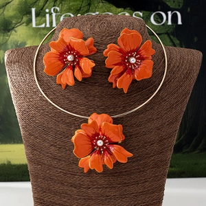 Detail view of orange floral enamel jewelry set with pearls on a brown display stand