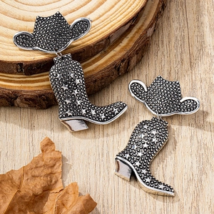 Detail of vintage silver cowboy hat and boot earrings with star relief on wooden surface