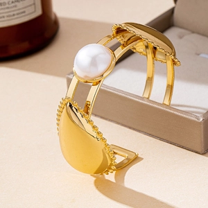 Detalle de un brazalete abierto dorado vintage con una gran perla blanca y gotas de oro