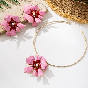 Detail of pink floral jewelry set with enamel petals and pearl center on stony backdrop