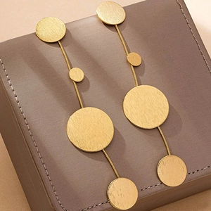 Detailed macro view of long golden tiered drop earrings with matte textured metal disks