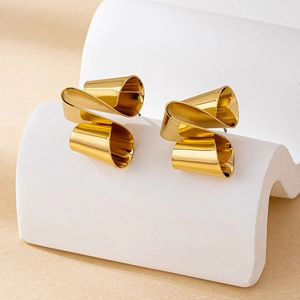 Detailansicht goldener gedrehter geometrischer Ohrstecker auf weißem Displayständer