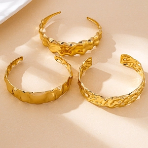 Détail de trois bracelets ouverts dorés aux textures ondulées et martelées élégantes