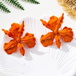 Detail of bright orange oversized geometric flower earrings on a seashell white tray