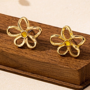 Vista detallada de pendientes de flores doradas con pétalos calados y cristal amarillo
