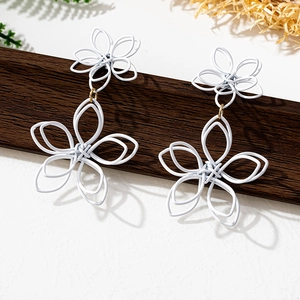 Detail view of large white floral earrings with matte finish and gold metal link