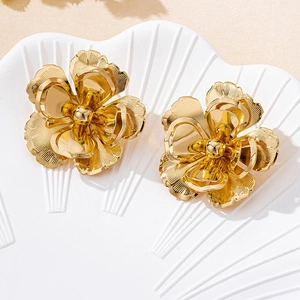 Macro shot of gold floral earrings with brushed texture on white shell tray