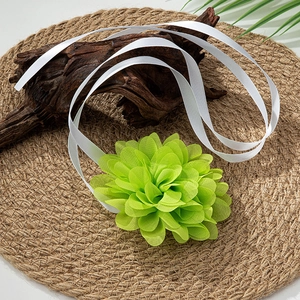 Close-up of light green tulle flower choker with long white silk ribbons on a rustic mat