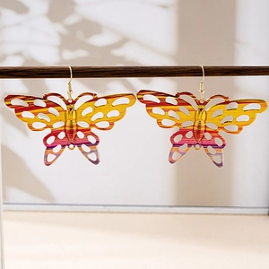 Detail view of colorful gradient butterfly drop earrings hanging on a wooden stand