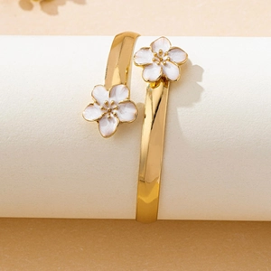 Détail du bracelet jonc doré ouvert orné de deux fleurs en émail blanc sur ruban plat