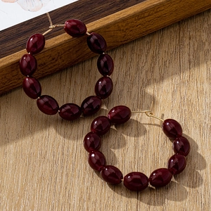Detalle de pendientes de aro con cuentas rojas y detalles dorados sobre madera rústica