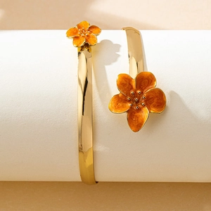 Gros plan détaillé d'un bracelet ouvert doré orné de fleurs en émail orange