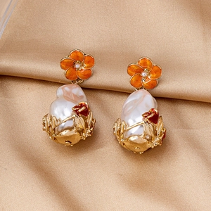 Detail of vintage drop earrings with orange enamel flower and oversized baroque pearl