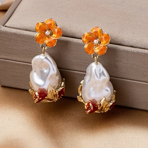 Detail of vintage flower earrings with orange glaze, pearls, and baroque style details