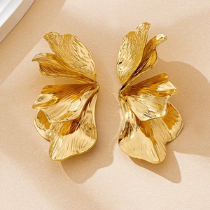 Dettaglio di orecchini a fiore dorati con petali metallici strutturati in stile lusso