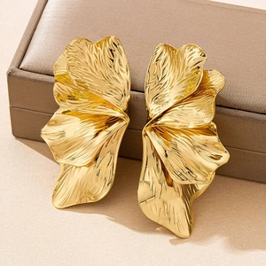 Dettaglio macro di orecchini a petalo d'oro con texture spazzolata e onde metalliche