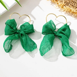 Dettaglio di orecchini a cuore dorati con grandi fiocchi in tessuto verde smeraldo su bianco