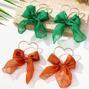 Dettaglio di orecchini a fiocco in tessuto verde e arancione con ganci a cuore dorati