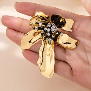 Detailed close-up of a large gold floral brooch with hammer texture and crystal center