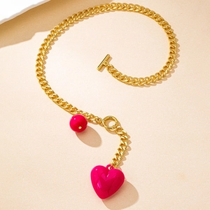 Detail of gold OT buckle necklace with a red sphere and pink heart pendant