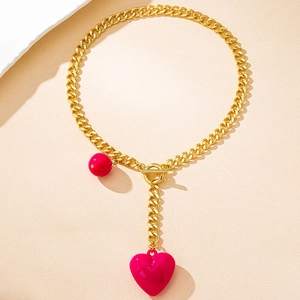 Detail of gold Cuban chain with OT clasp featuring a red sphere and pink heart charm
