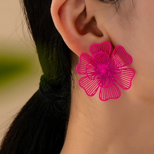 Primer plano de pendientes de flores huecas en rosa vibrante con intrincado patrón de calado