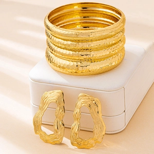Detailed macro view of four hammered gold bracelets and hollow wave earrings on jewelry box