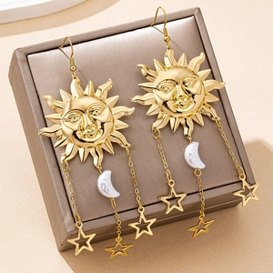 Detail of golden sun-shaped drop earrings with star and moon charms on a jewelry box