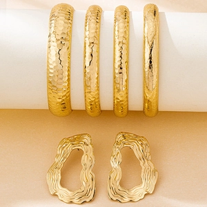 Detail of vintage gold textured bangles and wavy earrings set on beige stand