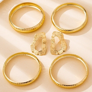 Detail of four hammered gold bangles and abstract fluid earrings on beige background
