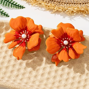 Detail view of orange floral earrings with red gradient petals and white pearl centers