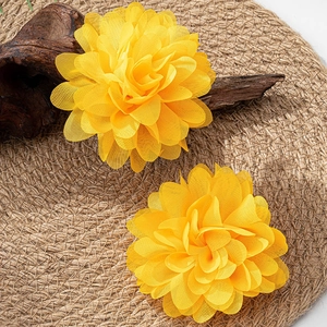 Detail von gelben Stoffblumen-Ohrringen auf gewebter Matte mit Naturholzdeko