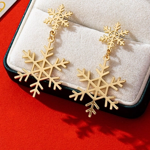 Detailed close-up of golden snowflake dangle earrings in a beige jewelry gift box