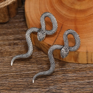 Gothic silver snake earrings with detailed scale texture on a natural wooden background