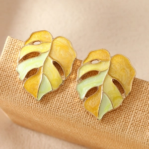 Boucles d'oreilles feuille monstera en émail jaune et vert sur un support texturé