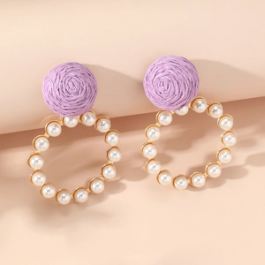 Elegant purple woven earrings with a gold ring and white pearls on peach background