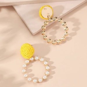 Detail of yellow woven stud earrings with gold rings and white pearl accents