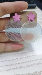 Detailed view of pink star and acrylic disco ball earrings held for display
