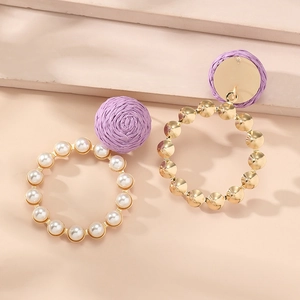 Detail of purple woven ball earrings with gold rings and inlaid pearls on stone