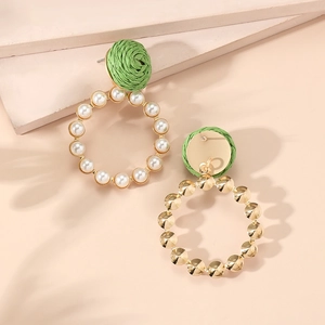 Detail view of gold earrings with green woven tops and pearls on neutral background