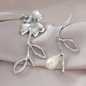 Detail van vintage zilveren oorbellen met asymmetrische bloem en parel op satijnen stof