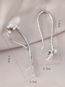 Detalle de pendientes asimétricos con perlas y medidas sobre fondo de seda suave